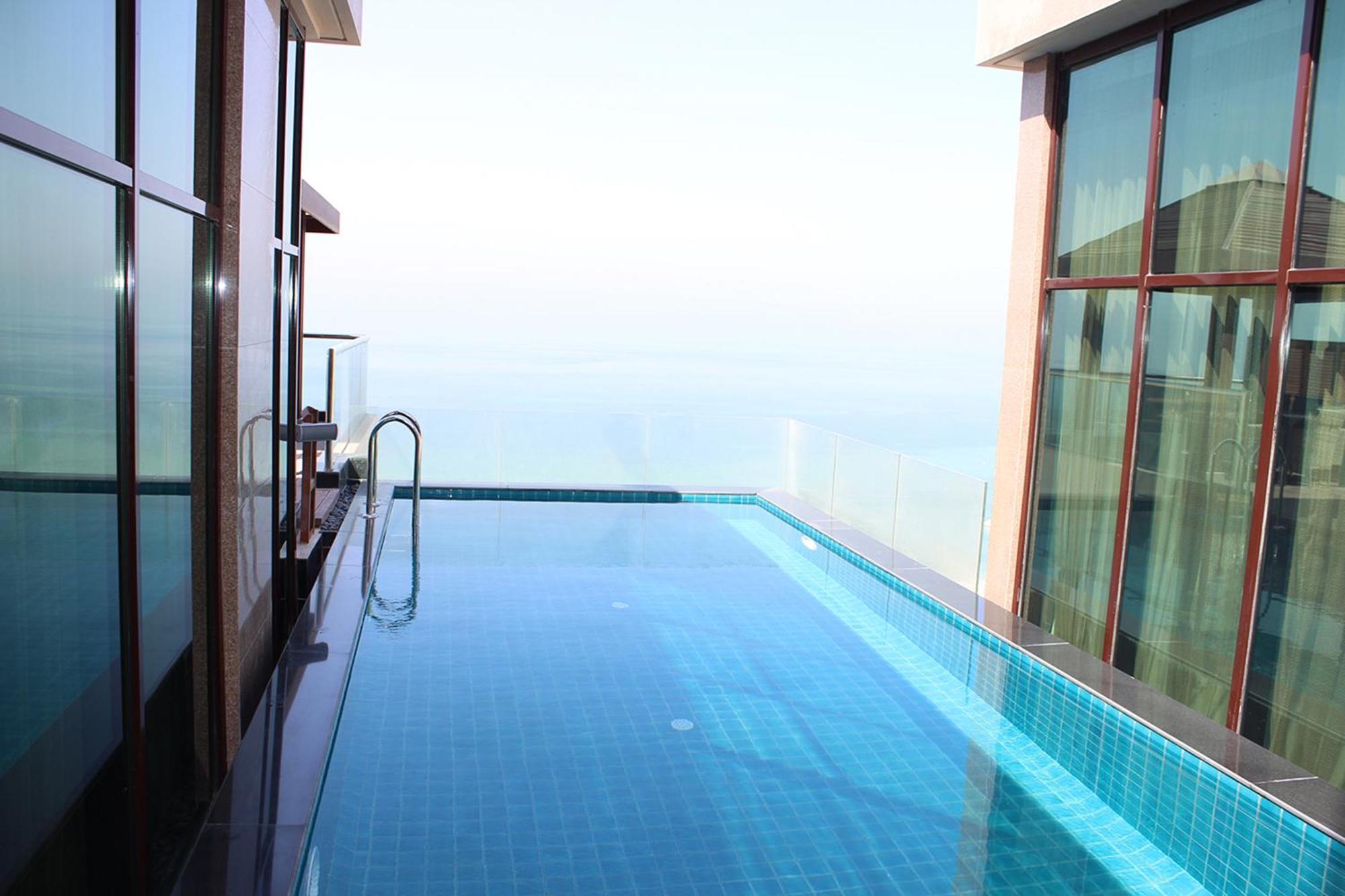 Lagoona Beach Luxury Resort And Spa Manama Exterior photo The photo shows an infinity pool situated on a balcony or rooftop, with a clear view extending to the horizon. The pool has a sleek design with blue tiles, and it appears to be reflecting the sky. There is a ladder on one side for access into the poo