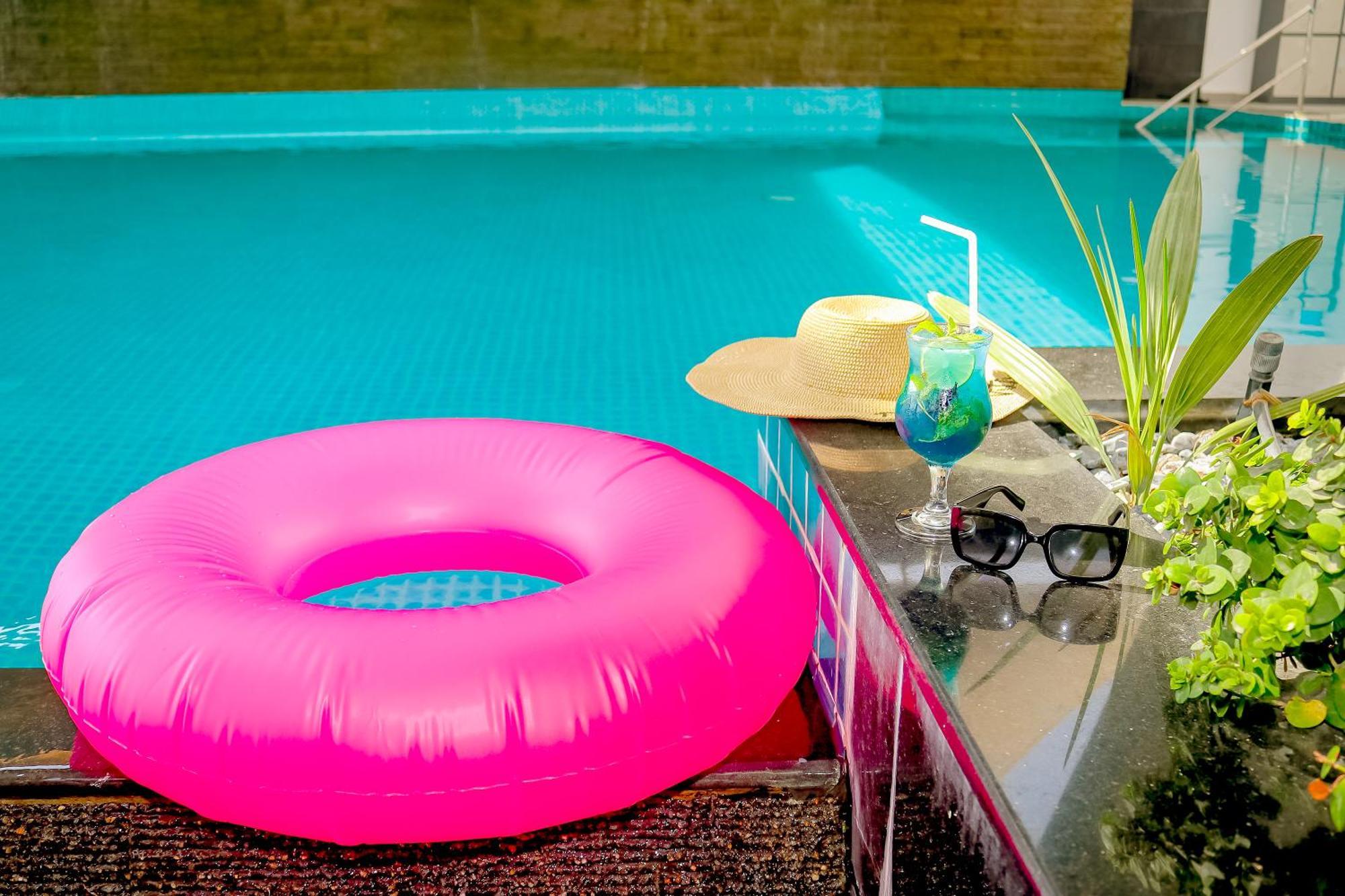 Lagoona Beach Luxury Resort And Spa Manama Exterior photo The photo shows a vibrant and inviting scene by a swimming pool. In the foreground, there is a large pink inflatable float and a stylish straw hat. Next to the float, a refreshing cocktail in a glass is displayed, complete with a straw and garnishes.