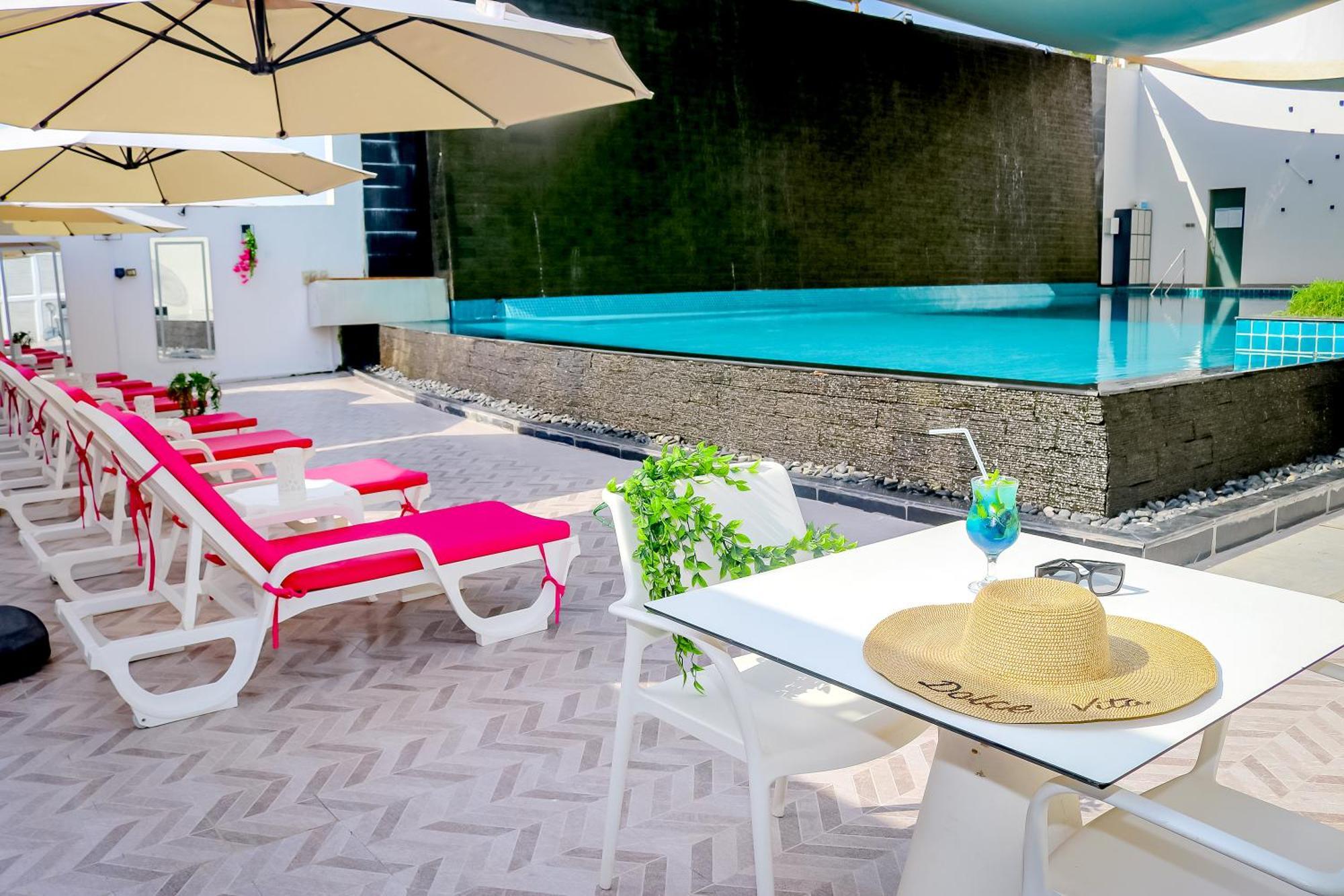 Lagoona Beach Luxury Resort And Spa Manama Exterior photo The photo shows a sunny poolside area with bright red lounge chairs arranged neatly beside a swimming pool. There are large beige umbrellas providing shade. A small table is set up with a straw hat and a colorful drink, suggesting a relaxed, tropical