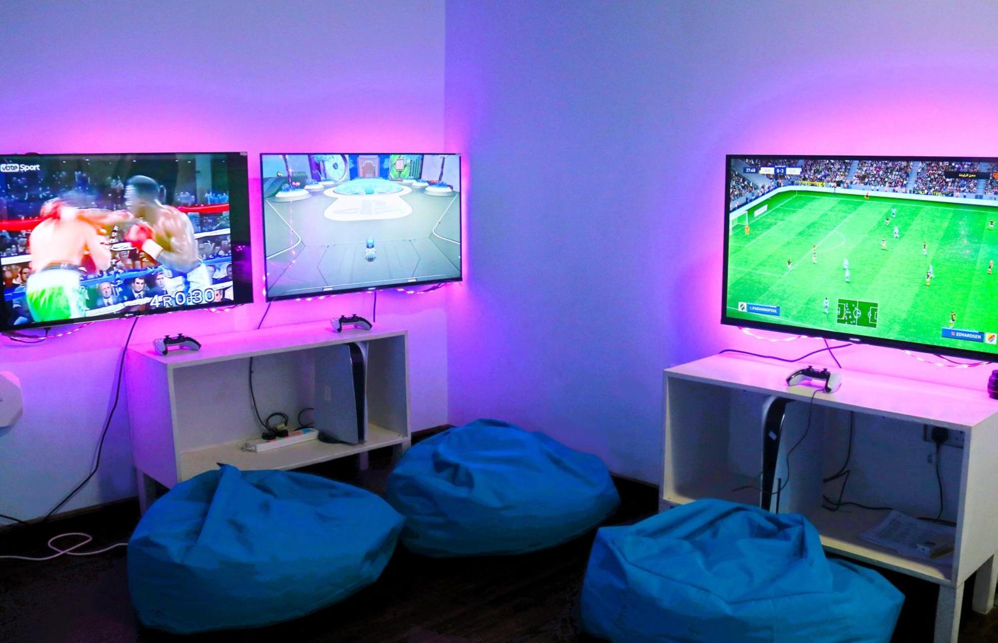 Lagoona Beach Luxury Resort And Spa Manama Exterior photo The photo shows a gaming area featuring three televisions mounted on the wall, displaying different games. Two of the TVs are showing gaming scenes, with one depicting a boxing game and the other showing a vibrant game environment. The third TV displ