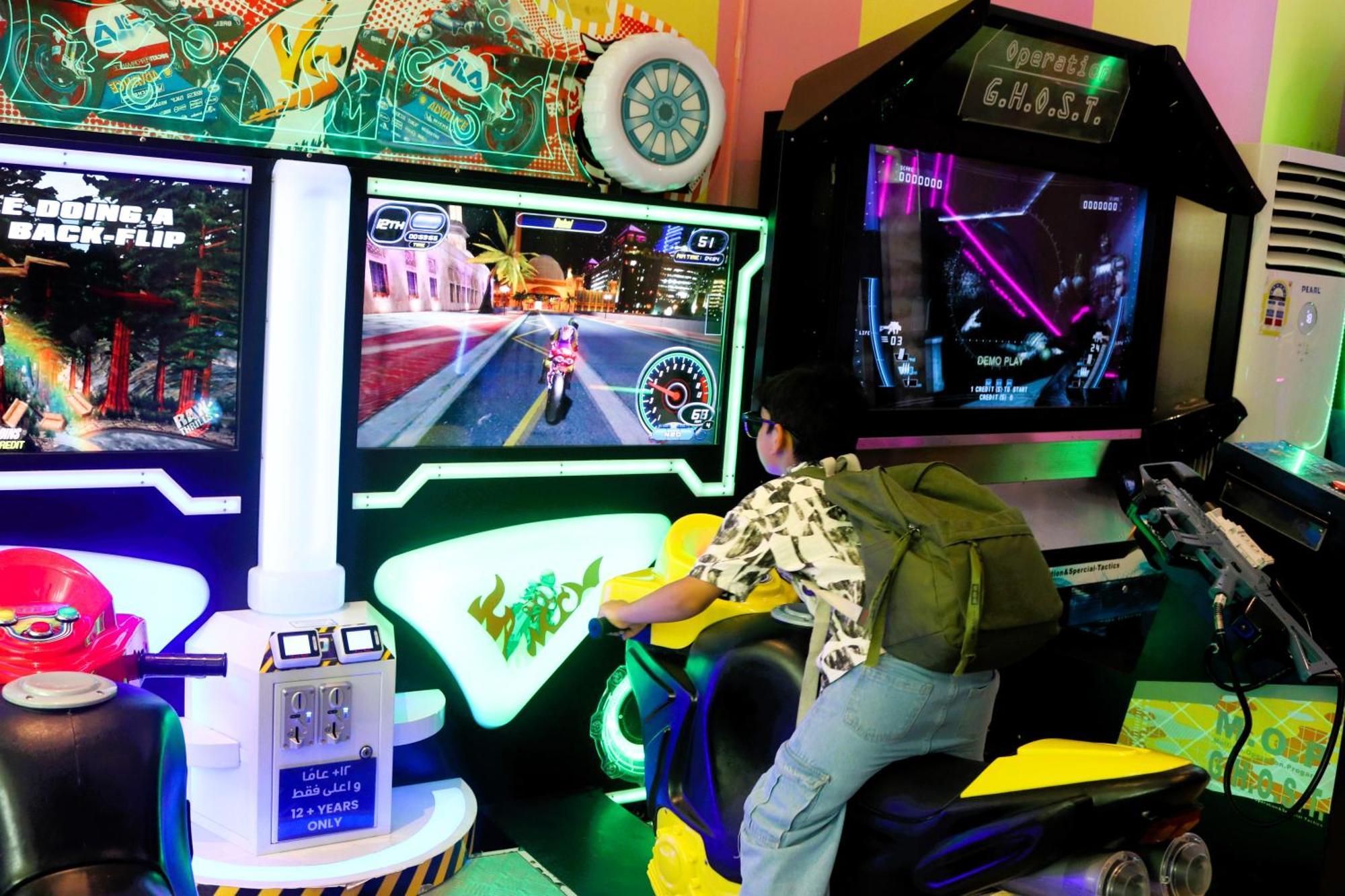 Lagoona Beach Luxury Resort And Spa Manama Exterior photo The photo shows a person playing an arcade motorcycle racing game. They are seated on a motorcycle-shaped seat, actively engaging with the game displayed on the screen in front of them. The screen shows a vibrant racing scene with streets and colorfu
