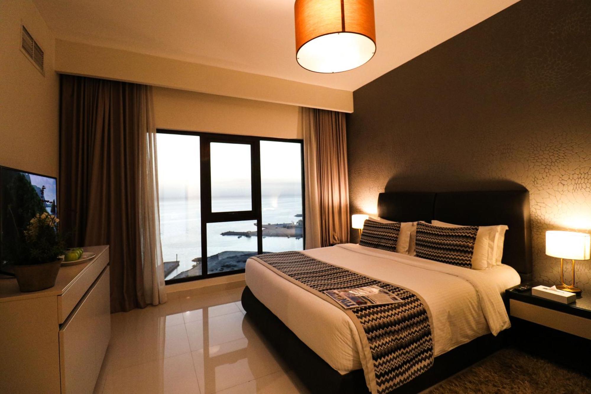 Lagoona Beach Luxury Resort And Spa Manama Exterior photo The photo shows a modern hotel room featuring a neatly made bed with decorative pillows. The room has a stylish design with a dark accent wall and a large window that offers a view of the outdoors. Natural light comes in, giving the space a bright an
