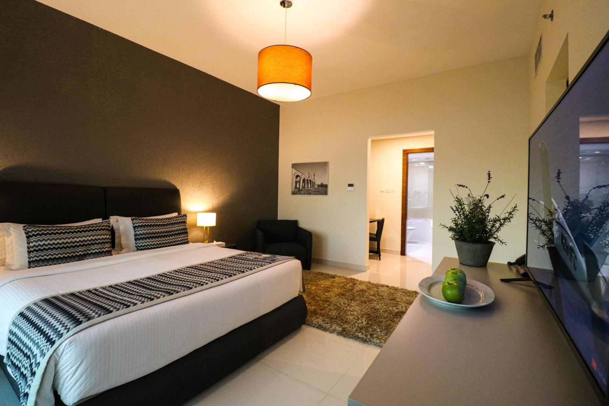 Lagoona Beach Luxury Resort And Spa Manama Exterior photo The photo shows a modern hotel room. It features a large bed with a neatly made white and dark-colored duvet. On either side of the bed, there are bedside tables with lamps. The wall behind the bed is painted in a dark color, creating a contrast with
