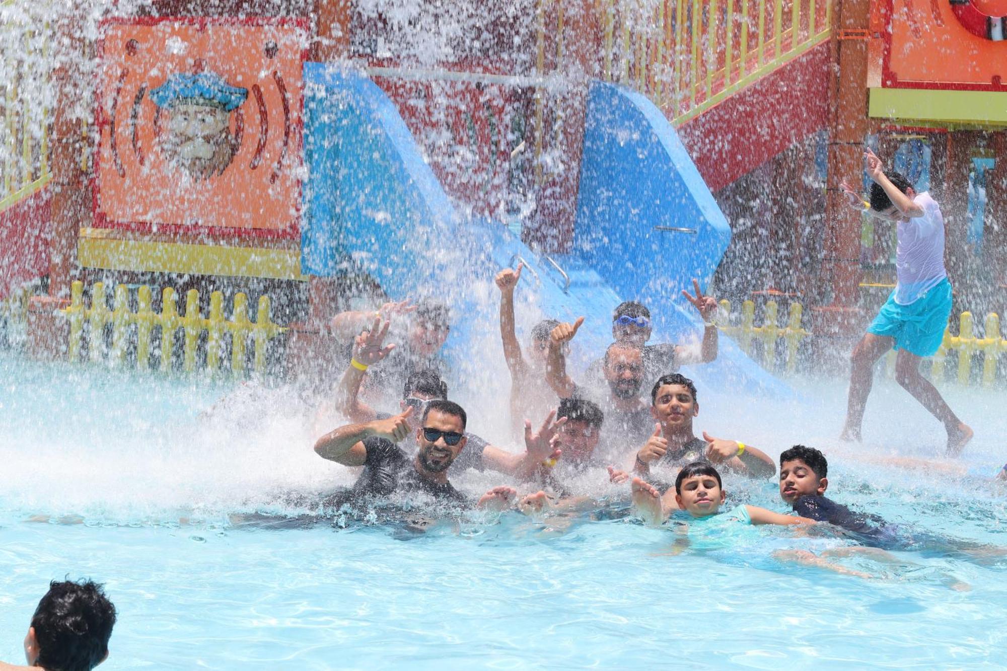 Lagoona Beach Luxury Resort And Spa Manama Exterior photo The photo shows a lively scene at a water park or pool area. Several people, including adults and children, are enjoying themselves in the water, splashing and posing for the camera. Water is cascading down, creating a refreshing atmosphere. In the b