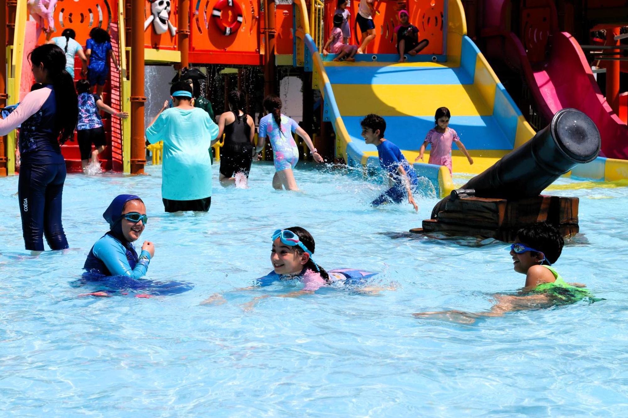 Lagoona Beach Luxury Resort And Spa Manama Exterior photo The photo shows a vibrant water park scene with several children playing in a shallow pool. Some are swimming and splashing around, while others are playing on colorful slides in the background. The atmosphere is lively and cheerful, with kids of var