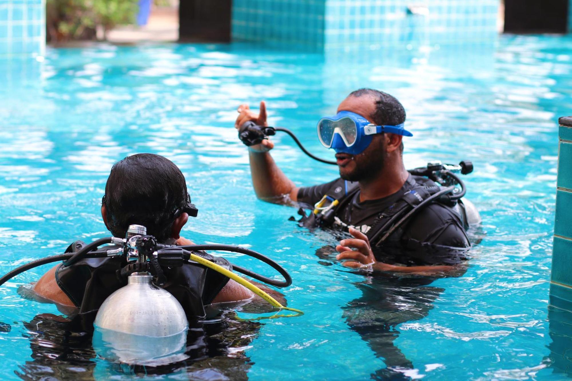 Lagoona Beach Luxury Resort And Spa Manama Exterior photo The photo shows two divers in a pool. One diver is wearing a scuba mask and is speaking to the other diver, who is also equipped with scuba gear. They appear to be engaged in a discussion, possibly related to diving instructions or safety. The water 