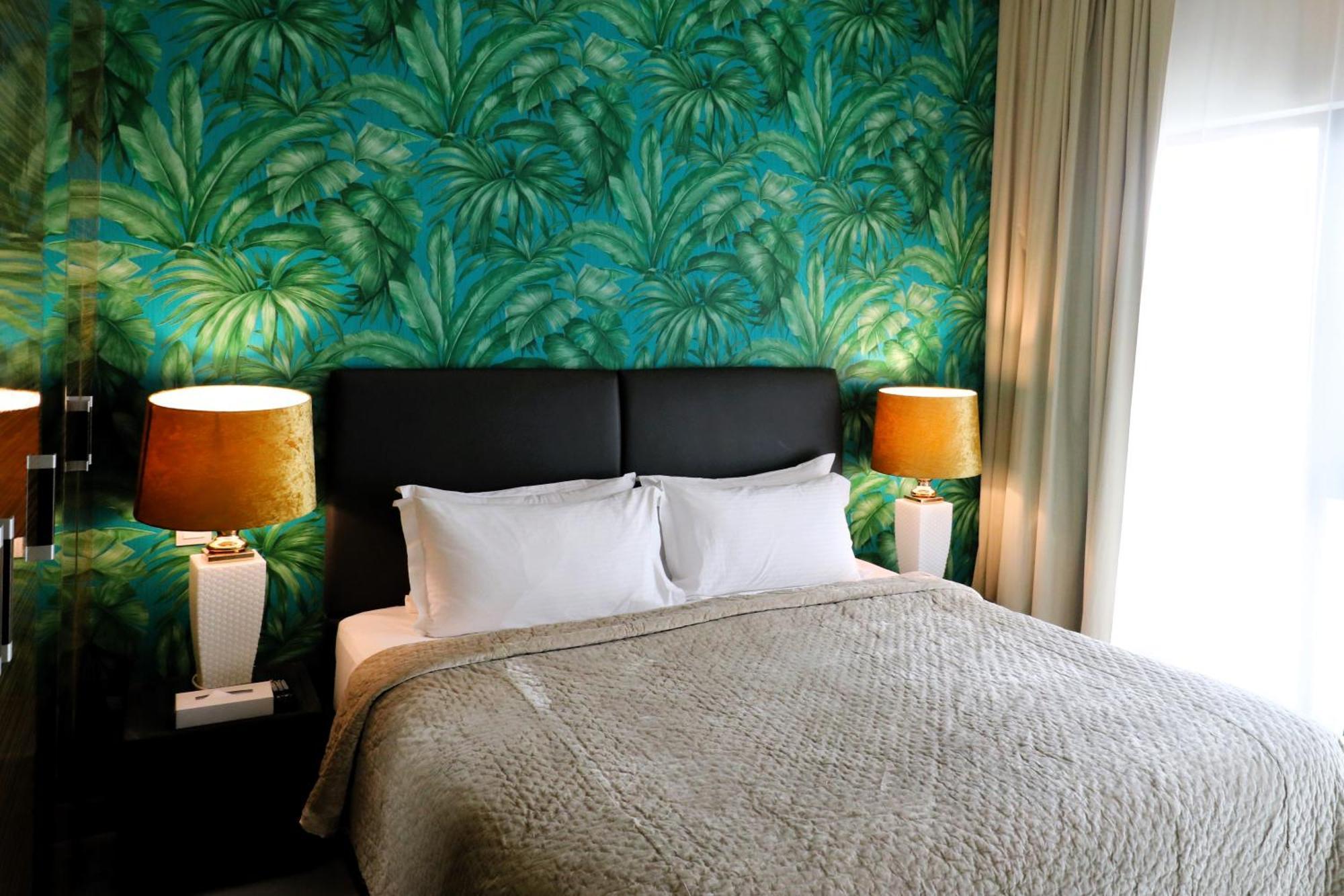 Lagoona Beach Luxury Resort And Spa Manama Exterior photo The photo shows a stylish bedroom featuring a large bed with white pillows and a gray blanket. The headboard is upholstered in black, providing a modern touch. Behind the bed, there is a vibrant green wallpaper with a tropical leaf pattern, adding a 