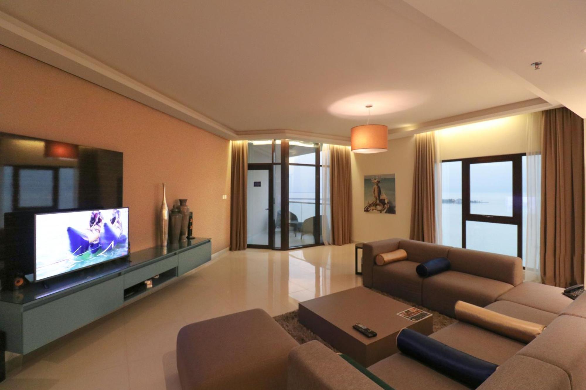 Lagoona Beach Luxury Resort And Spa Manama Exterior photo The photo shows a modern living room with a sleek design. There is a large wall-mounted television on a contemporary entertainment unit, with decorative items placed beside it. The room features a comfortable sectional sofa in light tones, with a cof