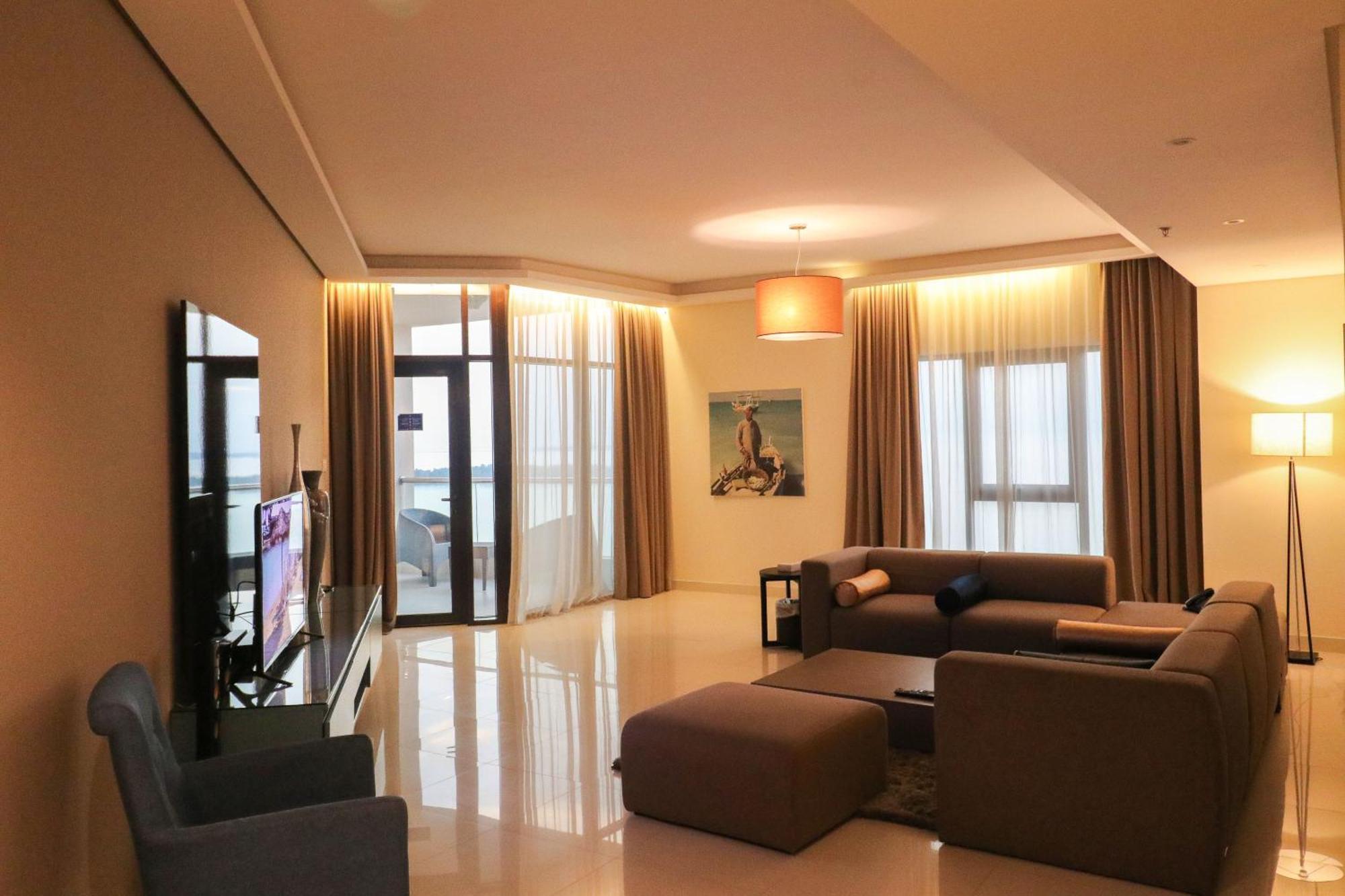 Lagoona Beach Luxury Resort And Spa Manama Exterior photo The photo shows a modern living room with a spacious and elegant design. It features a large couch in neutral tones, a soft ottoman, and a stylish coffee table. The walls are painted in a light color, and there are large windows with sheer curtains a