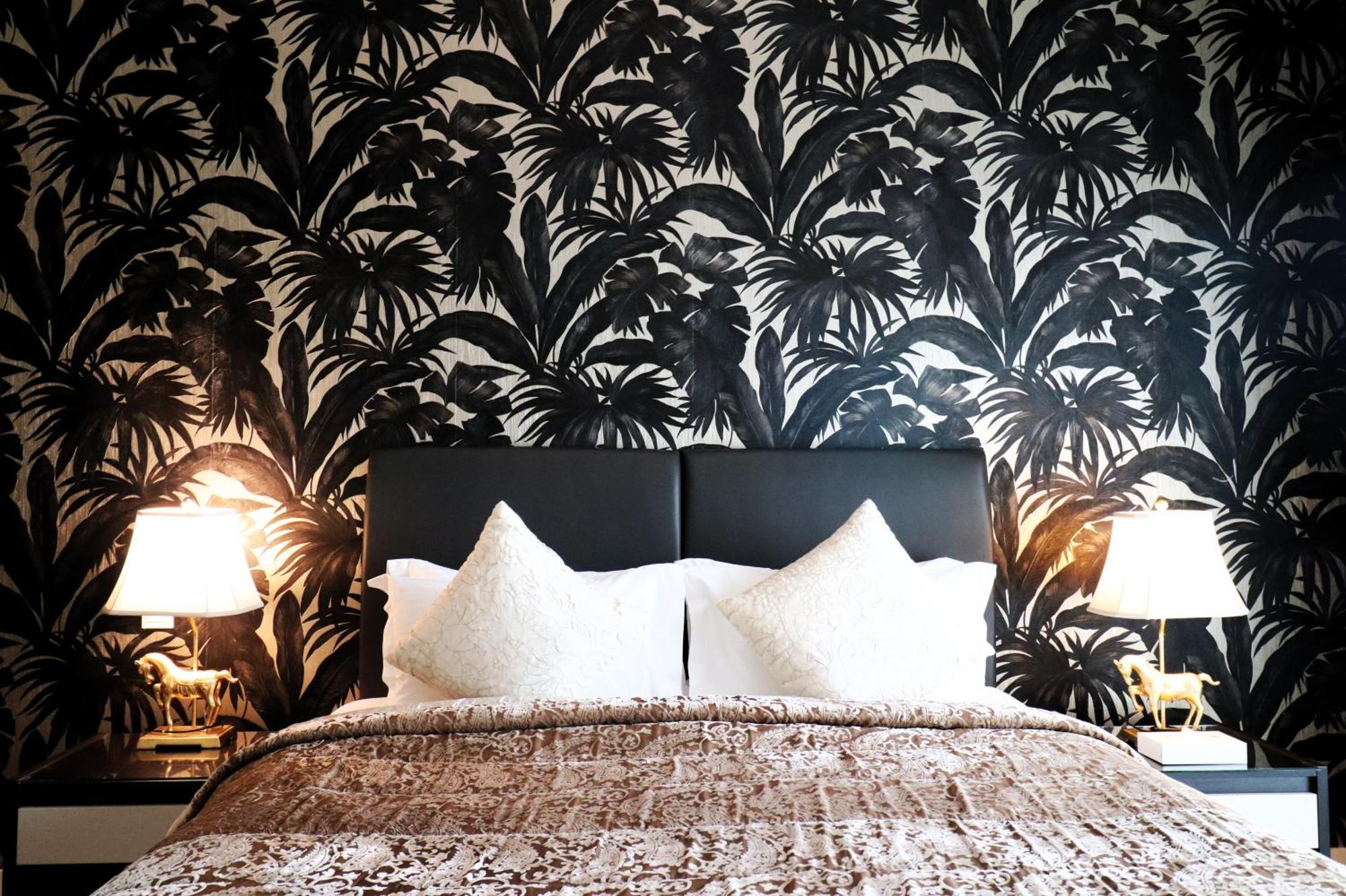 Lagoona Beach Luxury Resort And Spa Manama Exterior photo The photo depicts a stylish bedroom featuring a distinctive wall covered in a black and white tropical foliage wallpaper. The bed has a modern black headboard and is adorned with white pillows, creating a clean and elegant look. A textured brown thro