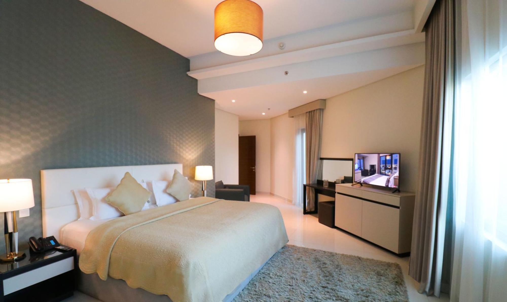 Lagoona Beach Luxury Resort And Spa Manama Exterior photo The photo shows a modern hotel room featuring a large bed with a light-colored blanket and decorative pillows. The walls are painted in a subtle shade, and there is a textured accent wall behind the bed. On one side, a bedside lamp provides warm ligh