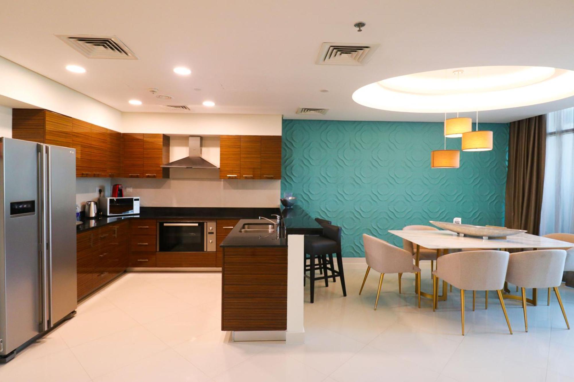 Lagoona Beach Luxury Resort And Spa Manama Exterior photo The photo shows a modern kitchen and dining area. The kitchen features wooden cabinets, sleek appliances including a stainless steel refrigerator, microwave, and an oven. There is a dark countertop and a small breakfast bar with high stools. The wall
