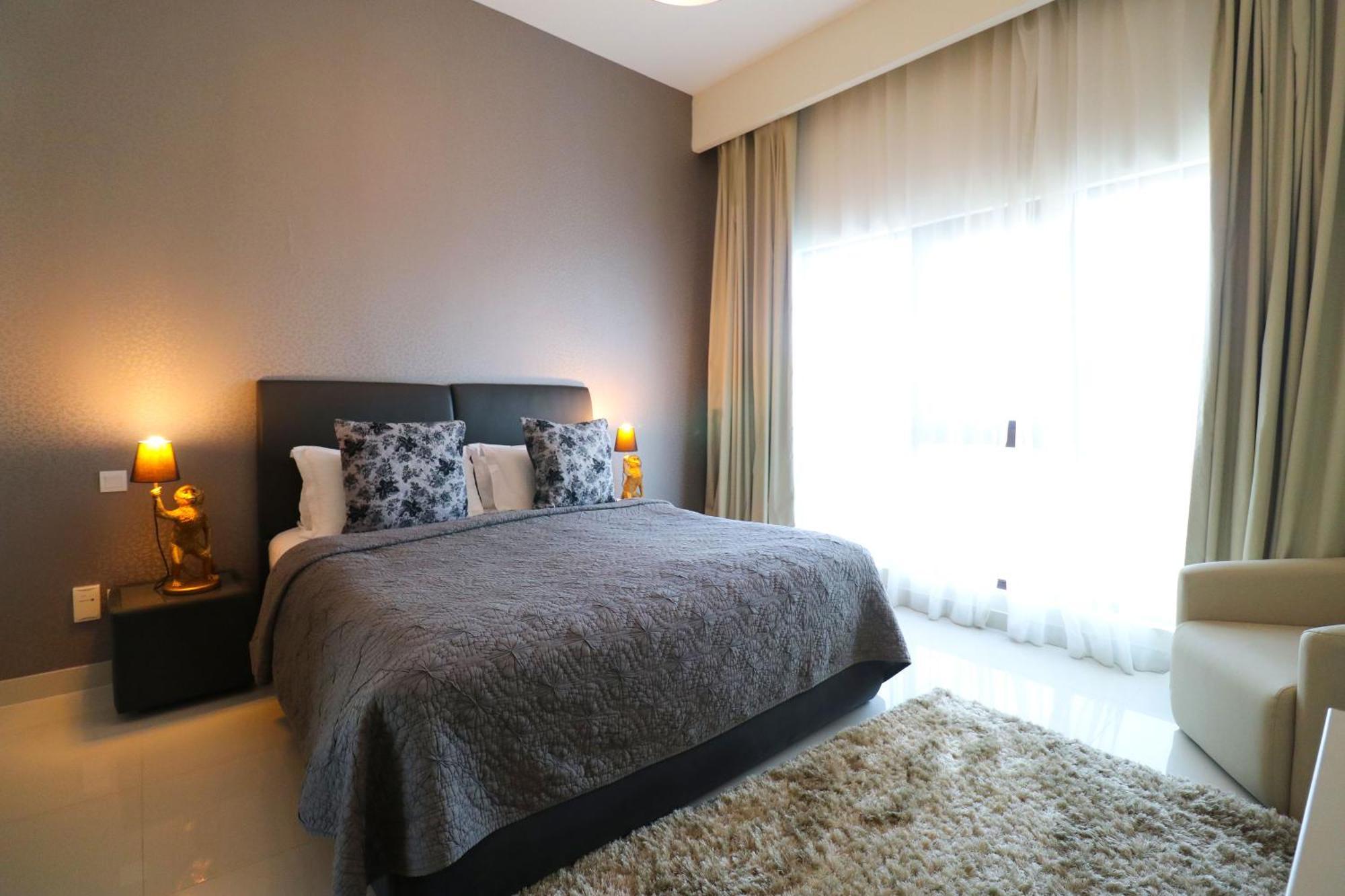 Lagoona Beach Luxury Resort And Spa Manama Exterior photo The photo shows a stylish bedroom with a modern design. It features a large bed with a dark gray bedspread and decorative pillows. On either side of the bed are two wooden nightstands, each with a lamp. There is a large window covered with light, flo